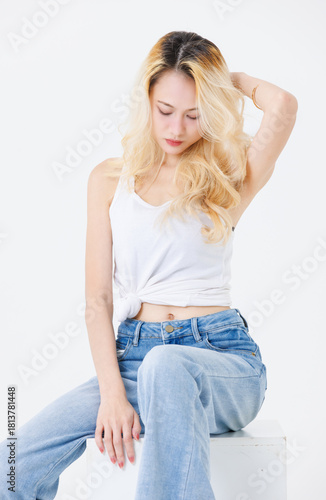 Asian confident beautiful attractive woman blonde long hair sit on cube box wear sleeveless top jeans on white background studio, portrait lifestyle fashion street outfit trendy style look at camera.