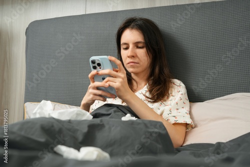 Sick woman using smartphone in bed