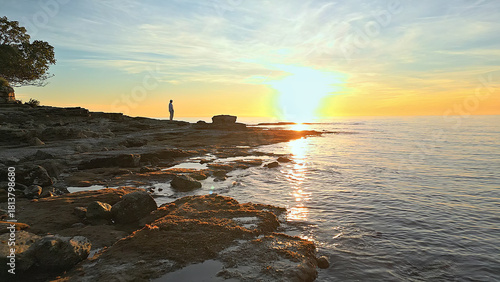 Fotografie A lone figure stands on rocky shores at sunset, gazing at the horizon