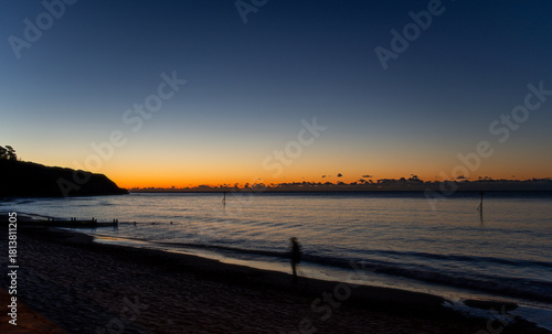 A solitary man walks along a beach at sunrise. Subtle motion blur. Solitude and relaxation. Coastal walk. Mental health image.