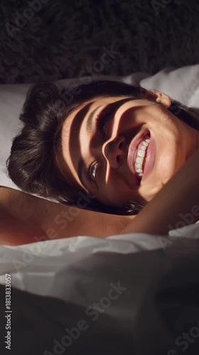 A woman enjoys the gentle morning light while waking up in her bed