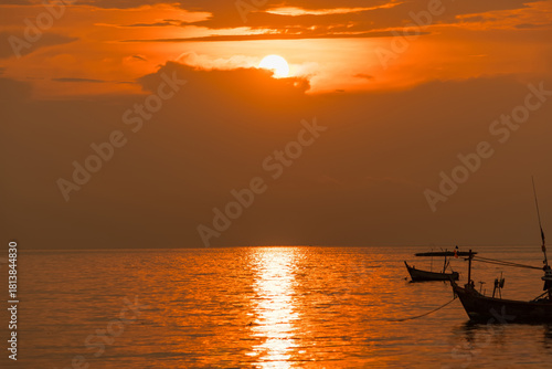 Fishing boats floating on calm sea during vibrant orange sunset with dock in foreground and golden reflections on water surface