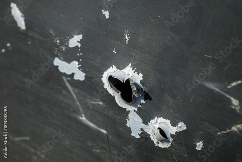 Close up detail view of a jagged shrapnel hole in the dirty scratched green metal door of a mil vehicle damaged by heavy artillery or mortar shelling during dangerous war combat action on the street