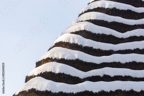 Close up view of a traditional reed thatched roof covered with thick white snow layers against the blue sky creating a beautiful graphic abstract geometric winter texture background
