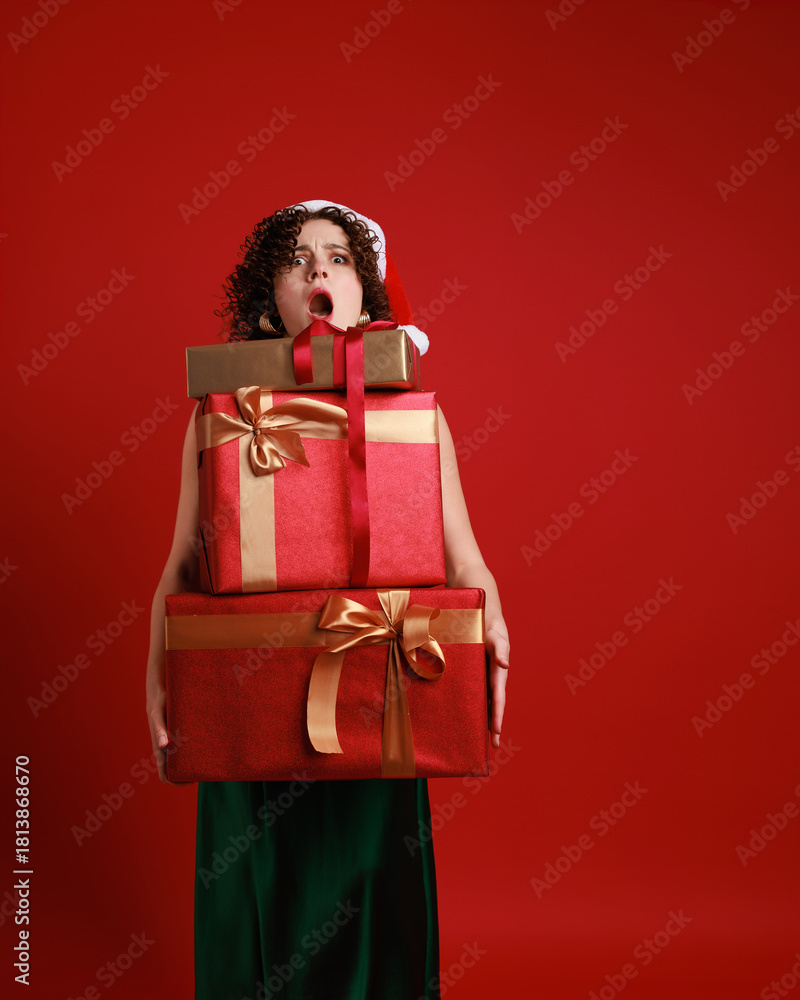 Φωτογραφία Elegant Christmas photo of a young woman in green satin dress and Santa hat standing with many gift boxes