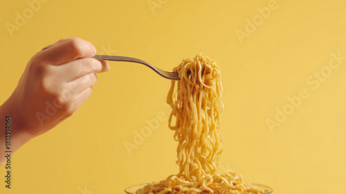 A hand holding a fork with noodles against a bright yellow background view