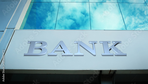 Prominent bank sign on a sleek, modern financial building, featuring striking cloud reflections in the glass windows, symbolizing finance, security, wealth, and corporate architecture