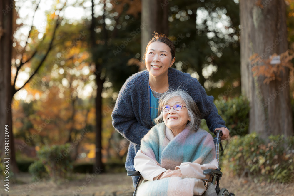 Fototapeta premium An elderly woman in a wheelchair taking a stroll amid the beautiful autumn foliage, accompanied by a caregiver and someone resembling her daughter.