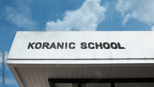 Koranic School sign on a building against a clear blue sky, symbolizing Islamic education, religious study, Quranic teaching, and faith learning