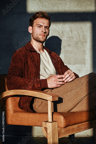 A thoughtful portrait of a man leaning forward with his hand near his face. His fitted casual outfit and neutral background create a refined, introspective editorial tone.