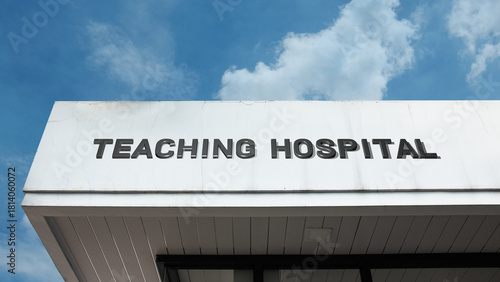 Teaching Hospital word signage on a medical or academic building under a blue sky, symbolizing healthcare, education, research, patient care, medical training, clinical practice, and institutional lea