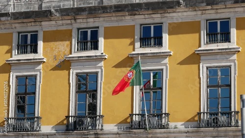 Portuguese national flag waving on the facade of a yellow building under bright sunlight in Lisbon, Portugal.