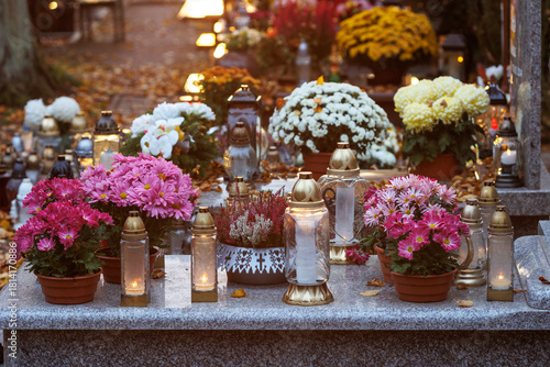 Kwiaty zdobiące nagrobki stanowią symbol pamięci, miłości i szacunku dla zmarłych. Jesienna kolorystyka w połączeniu z naturalnym światłem nadaje fotografii spokojny i nostalgiczny charakter.