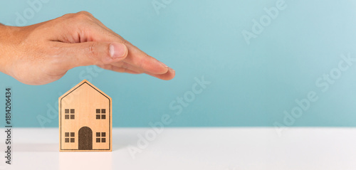 Protect property, mortgage, home, investment and financial savings concept. A man protecting roof over a miniature house with his hand symbolizing property and security insurance