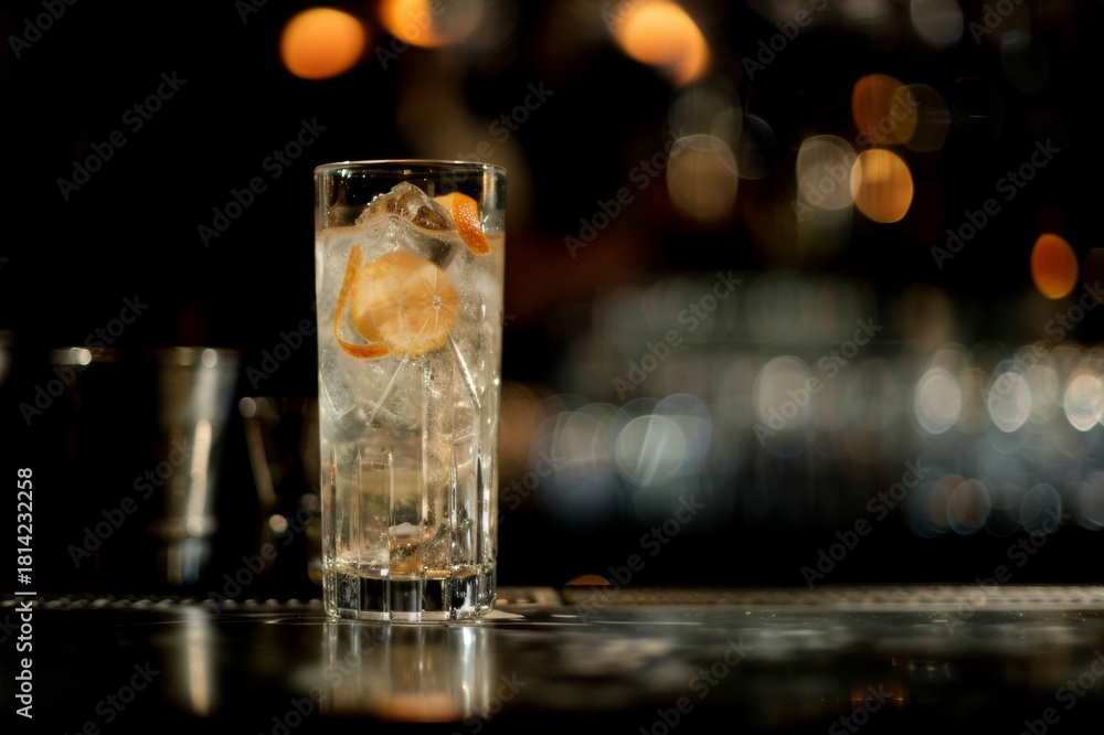 Fototapeta premium Cóctel elegante en vaso alto con twist de piel de naranja, Bebida de autor en barra de bar con iluminación cálida, Vaso de cristal tallado con bebida espirituosa y atmósfera nocturna
