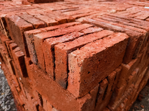 A full-frame close-up of a stacked red brick wall or pile, displaying the rough, weathered texture and repetitive pattern of masonry and construction material
