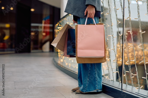 Woman's lower body and hand holding diverse shopping bags in a modern mall with festive string lights, concept of retail and consumerism