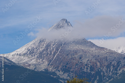 Snowy peaks in the High Tatras rise above silent slopes. Thin clouds drift slowly across the sharp summit in a calm arc. Cold light glints on rugged ridges that stretch toward distant valleys.