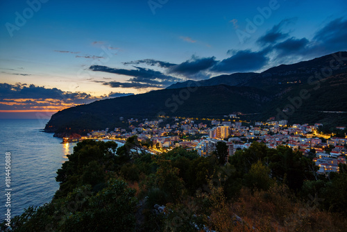Fototapeta Naklejka Na Ścianę i Meble -  sunset in small resort town Petrovac, Montenegro, beautiful sea view, city embankment with street lights, beach and mountains against sunset sky