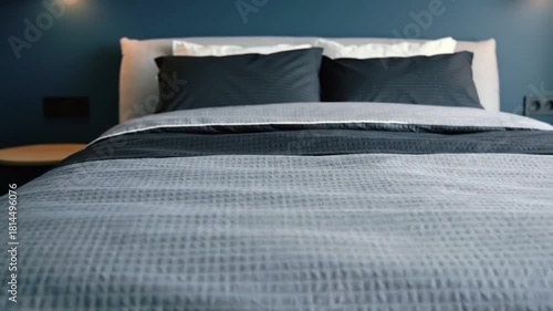 Cozy, well-made bed with dark pillows and grey bedding awaits rest.