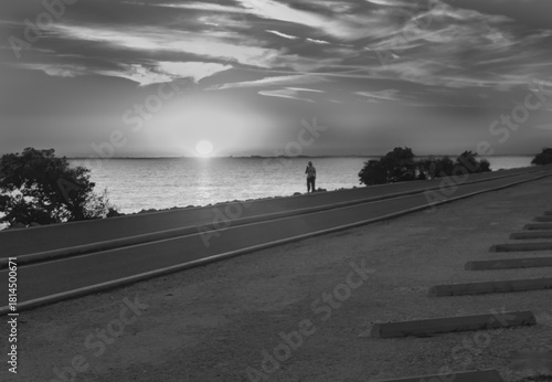 This photo captures a powerful silhouette of a person exercising along the Howard Frankland Bridge during a vibrant sunset. The dramatic twilight sky and glowing horizon create a striking backdrop
