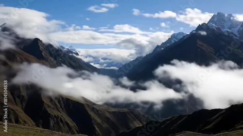 A mountain range with snow-capped peaks against a partly cloudy sky, with mist/clouds filling the valley below