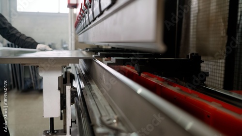 Close-up of an automated hydraulic press brake bending a metal sheet. An industrial worker is operating the machinery in a factory