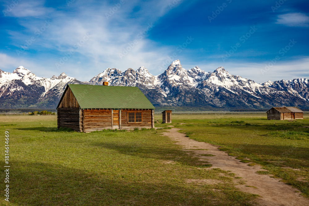 Obraz premium The snow covered Grand Teton Mountains in the background with a Mormon homestead and outhouse in Wyoming.