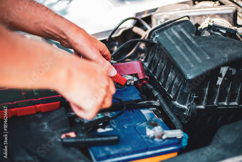 Under the hood of the car, the mechanic connects the clamp of the car jump starter to the terminal of the dead car battery