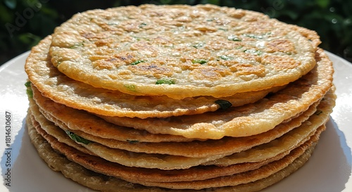 A close-up view of a tall stack of freshly made, golden-brown savory pancakes with green herbs.
