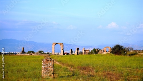 Obraz na plátně Ancient Roman ruins stand abandoned in a green field, featuring remnants of wall