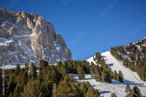 Sassolungo Rock with Snow Covered Ski Slope in South Tyrol. Winter Dolomites with Langkofel and Green Trees in Italy.