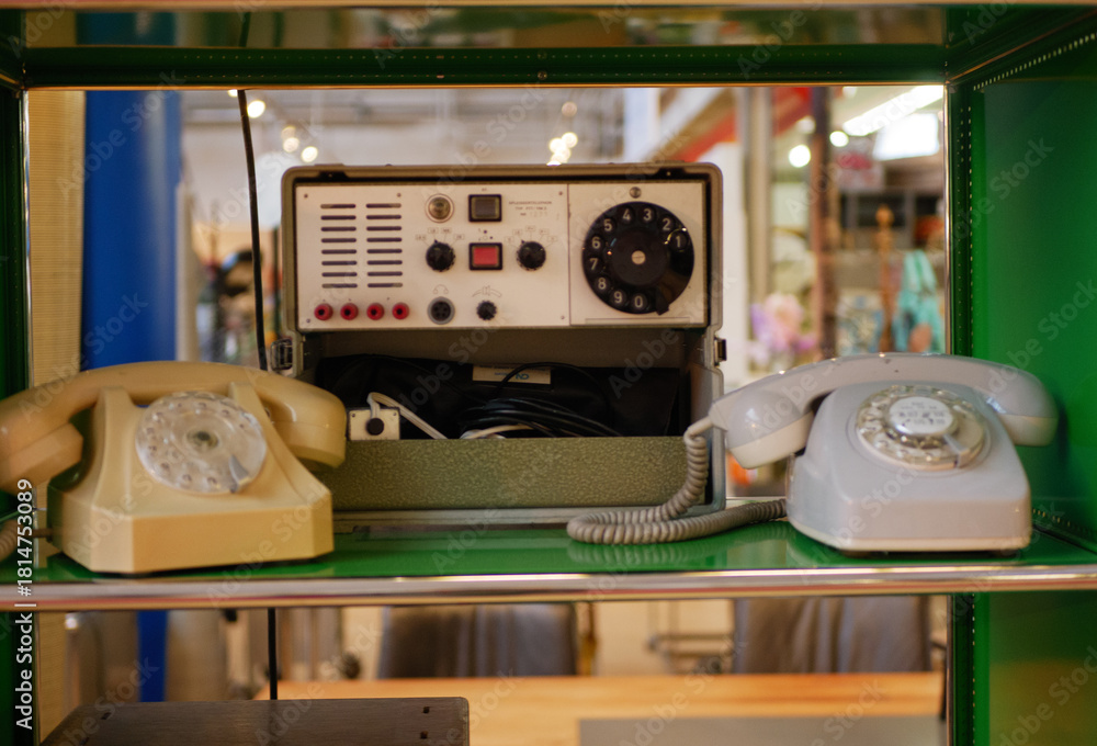 Fototapeta premium A vintage communication setup featuring rotary dial phones and an old control unit placed on a shelf. The equipment highlights classic technology and early communication systems. Ideal for
