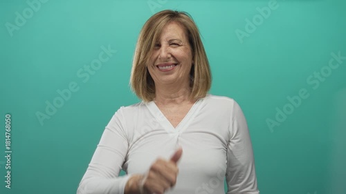 Wallpaper Mural Middle aged caucasian woman in white shirt winks at camera and gives thumbs up on a teal studio set; positivity empowerment confidence. Torontodigital.ca