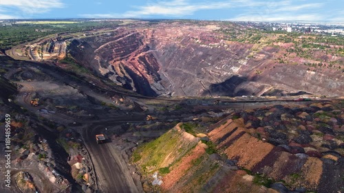 Heavy mining dump trucks driving along dusty haul roads inside vast iron ore open pit mine aerial view