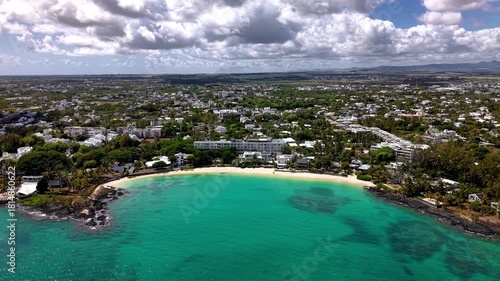 Cinematic drone shot approaching turquoise lagoon and white sand beach near coastal town in Mauritius