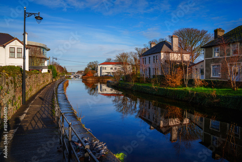 Vibrant, tranquil cityscape of Galway along the Eglington Canal with a view of traditional landmark architecture and trees lining the riverbank in Ireland.