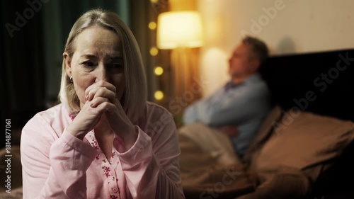 Sad middle-aged wife and husband sitting apart on bed, relationship crisis