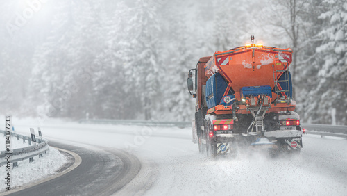 Snow plow clear and sprinkles snowy road in a snowstorm.