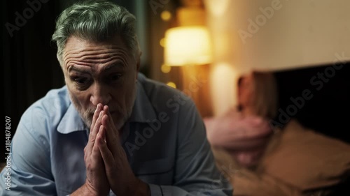 Upset middle-aged couple sitting separately on bed, signs of family conflict