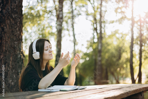 Young teen girl in headphones reading the Bible at a wooden table outdoors.