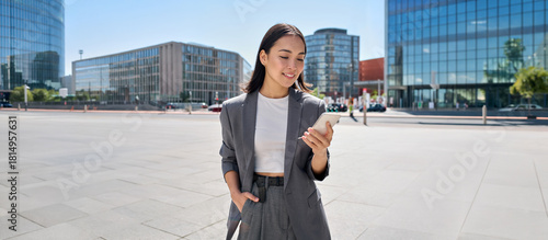 Obraz na płótnie Young smiling elegant Asian busy business woman leader wearing suit standing in big city using cell phone platform applications