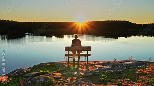 A man approaches, sits down on a bench on the cliff of river, and watches the sunset. The idea is reflection, solitude, privacy, travel.