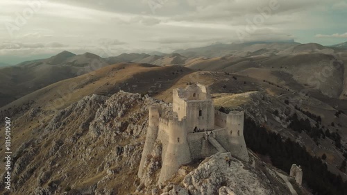 Cinematic drone shot of the ancient fortress of Rocca Calascio surrounded by the mountains of Abruzzo, Italy. Scenic hiking trail leading to the medieval castle on a rocky ridge at sunset.