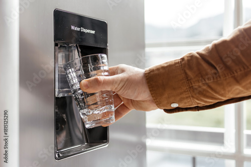 Canvas Print Hand of a person filling a clear glass with fresh water from a modern refrigerat