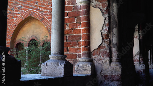 View of Riga Cathedral’s (Latvia) red brick facade framed by shaded corridor arches, blending Romanesque, Gothic, Baroque, and Art Nouveau styles.