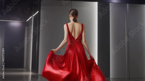 A model in a backless red gown walks through a sleek corridor. The flowing fabric captures a sense of dramatic movement and luxury. Generative AI.