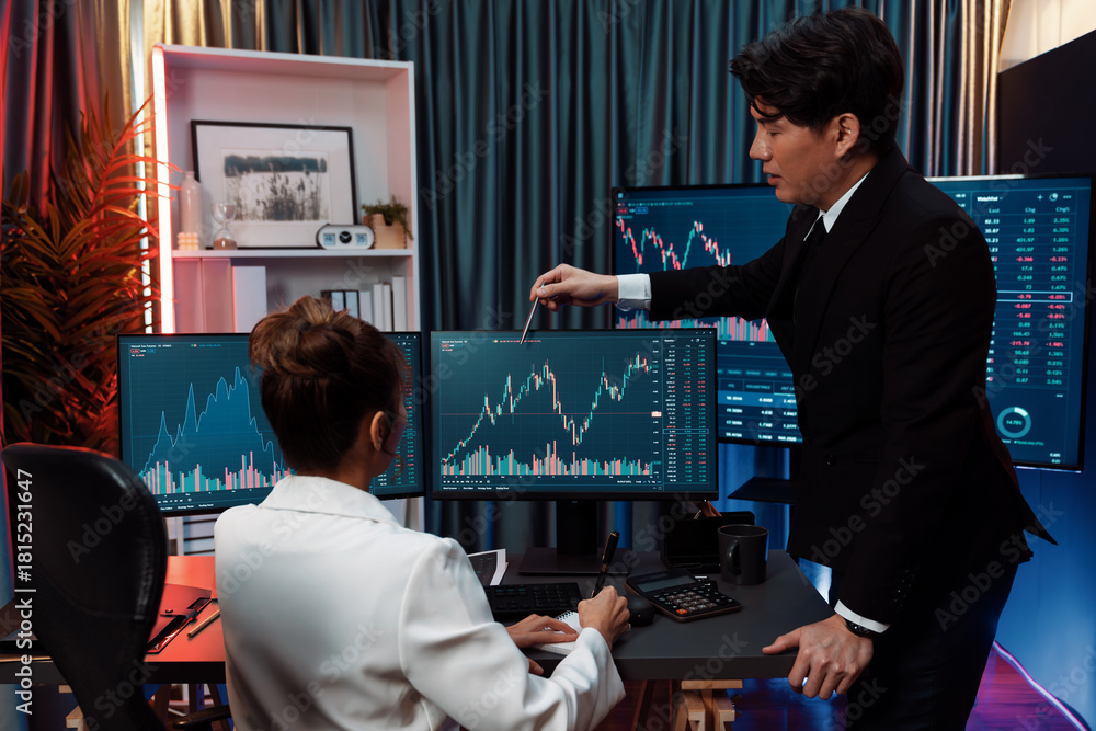 Obraz premium Trading business partners discussing on dynamic stock exchange statistic on pc screens taking note on paper, comparing with high or low point on currency graph at night neon modern office. Infobahn.
