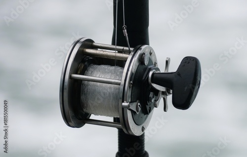Close-up view of a conventional saltwater fishing reel mounted on a rod, featuring silver metal components and tightly wound mono line.