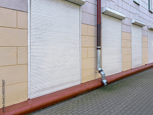 building facade with row of windows with closed roller shutters and rainwater downspout.